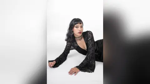 LilithBrooks poses in a black lace long-sleeve top and black skirt against a white background.