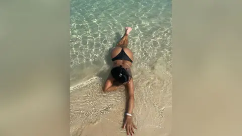 MissyJolie lies face down in clear shallow ocean water wearing a black bikini.