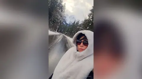 Woman in white faux fur coat and sunglasses enjoying a scenic snowy mountain road trip.