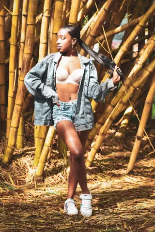 Young woman in denim shorts and jacket posing in a sunny bamboo forest setting.