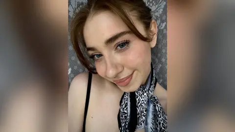 Smiling young woman with brown hair and blue eyes wearing a leopard print scarf in a soft indoor setting.
