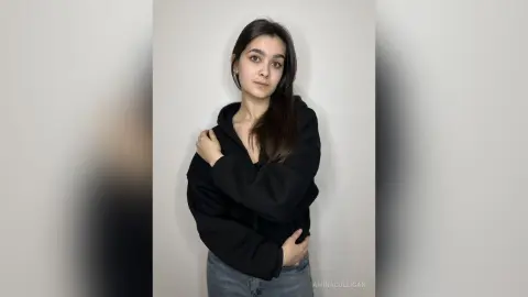 Young woman in a black oversized hoodie posing against a plain white background with a calm expression.