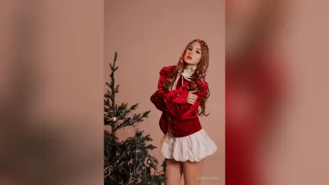 Red velvet outfit and white skirt on a woman posing by a Christmas tree in a festive holiday mood.