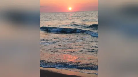 SaraTray captures a sunset over the ocean waves, with the orange sun reflecting on the moving water and beach sand.