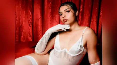 Elegant woman in a white satin bodysuit and long gloves posing against red velvet curtains.