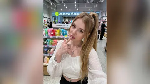 Blonde woman in a white polka dot blouse posing in a Zolotoe Yabloko beauty store with a soft, dreamy mood.