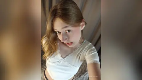 EvelinaMoorina wearing a white lace top and looking into the camera with her tongue out.