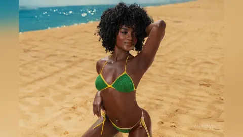 Smiling Black woman in a green crochet bikini relaxing on a sunny tropical beach.