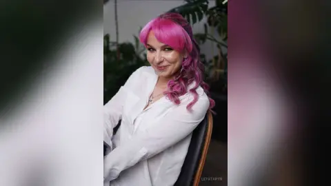 LeyaTaryn smiles while wearing a white button-down shirt and showing off her bright pink hair in an outdoor setting.