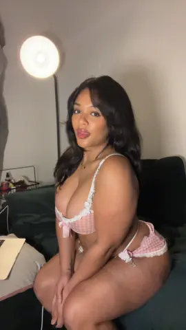 Hazelvalentine poses in a pink checkered lace bra and matching panties, showing off her curves while sitting on a dark couch.