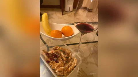 KimFu — KimFu sits at a table with a bowl of fruit, a banana, and a glass of red wine next to a dish of cooked crab.