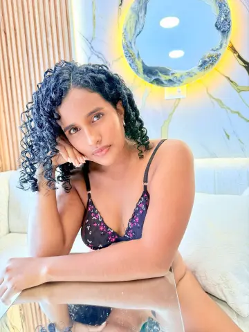 Curvy woman with curly hair in black floral lingerie relaxing on a white sofa in a bright modern room.