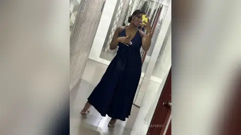 Smiling woman in a navy blue maxi dress taking a mirror selfie in a modern hallway.