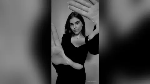 Moody black and white portrait of a woman in a black dress posing with hands near her face.