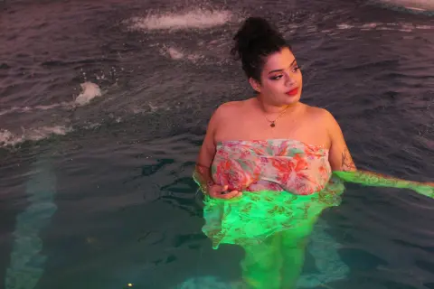Young woman in a floral strapless dress relaxing in a dark swimming pool at night.