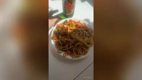 Delicious Chinese lo mein noodles with vegetables served on a white plate next to a cold Tsingtao beer bottle.