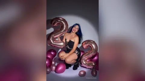 Smiling woman with blue hair in a black corset celebrating her 22nd birthday with pink balloons and rose gold balloons.
