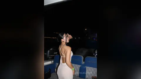 Elegant woman in a white backless evening dress enjoying a night boat ride under the dark sky.