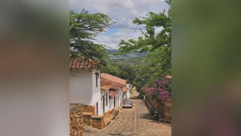 RossiNoleen's photo shows a narrow stone street lined with white buildings and red-tiled roofs, overlooking a lush green valley under a cloudy sky.