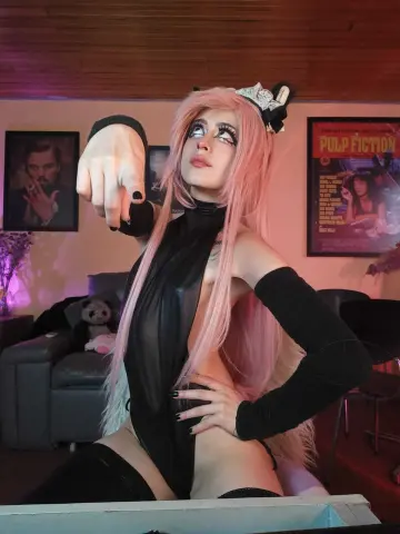 Cosplayer in black bodysuit and pink wig posing confidently in a living room with movie posters.