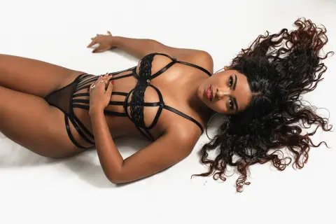Curvy woman in black strappy lingerie lying on a white background with voluminous curly hair.