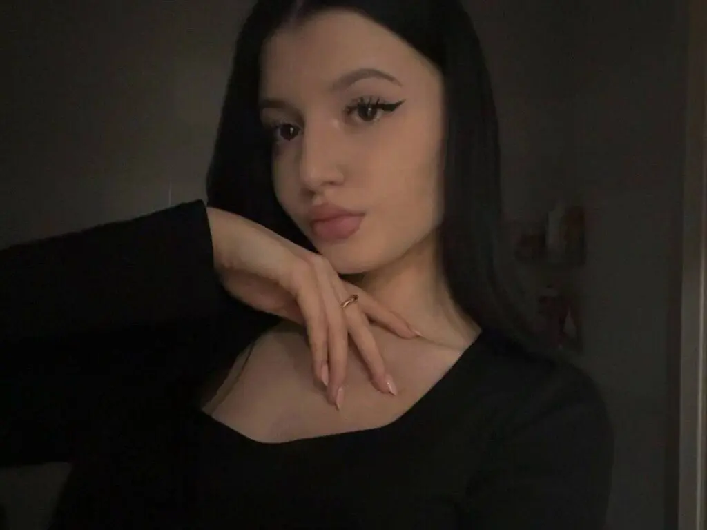 Young woman with long dark hair and winged eyeliner wearing a black top in a moody indoor setting.
