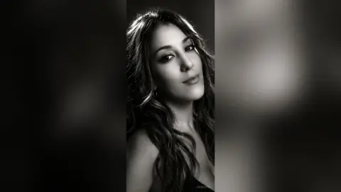 Close-up portrait of a woman with wavy hair in a moody black and white studio setting.