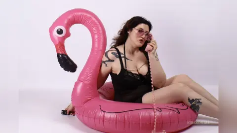 KiraKovall sits in a pink inflatable flamingo, wearing black lace lingerie and pink sunglasses while holding a pink telephone to her ear.