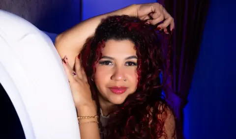 Smiling woman with curly red hair relaxing in a blue lit bedroom setting.