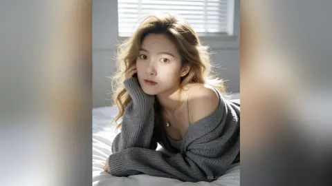 XiaJiaojiao poses on a white bed wearing a loose, grey knit sweater that slips off one shoulder, showing her neck and chest.