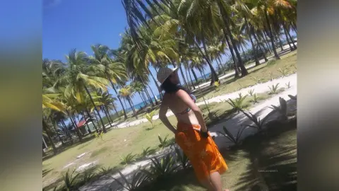 Woman in orange skirt and sun hat posing on a sunny tropical beach with palm trees.
