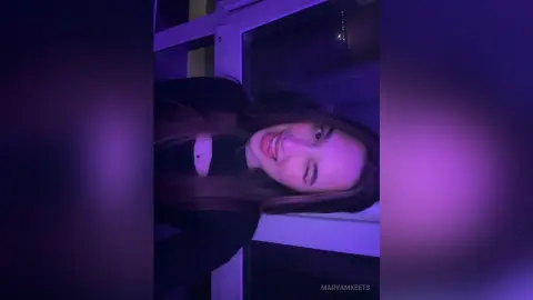 Smiling young woman in a black top under moody purple neon lighting indoors.
