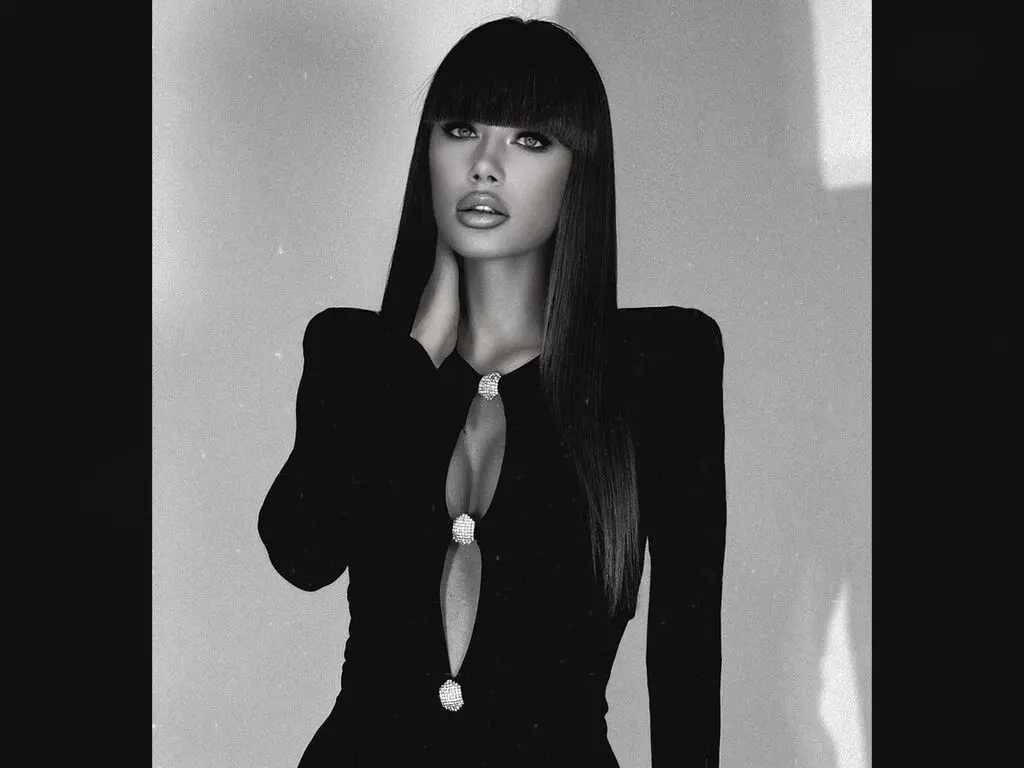 Elegant woman in a black cutout dress with long hair posing in a moody black and white studio portrait.