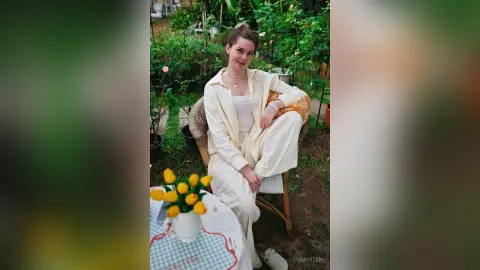 LiaMotzer sits on a chair outdoors wearing a white button-down shirt and matching white pants.