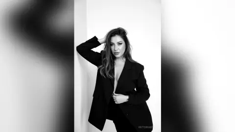 Elegant woman in a black blazer posing against a white wall in a moody black and white portrait.