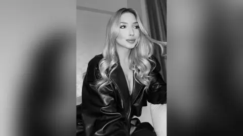 Blonde woman in a black leather jacket posing with a serene expression in a black and white portrait.