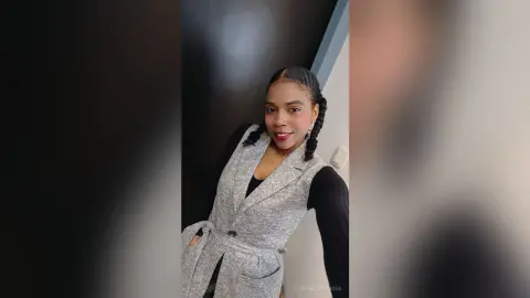 Smiling woman in a stylish grey waistcoat and black top posing in a modern indoor setting.