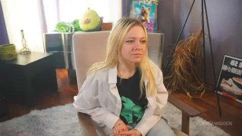 Blonde woman in a white shirt and black graphic tee sitting relaxed in a cozy, sunlit living room.