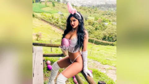 Woman in white bunny costume and gloves posing outdoors in a lush green hilly landscape.