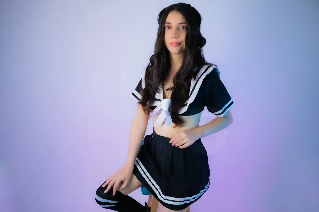 MegganParker has long dark hair and looks at the camera while resting her chin on her hand, wearing a pink polka-dot top.