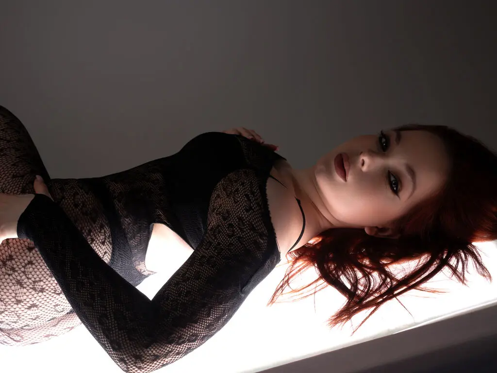 Elegant woman in a black lace bodysuit posing in soft, moody lighting.
