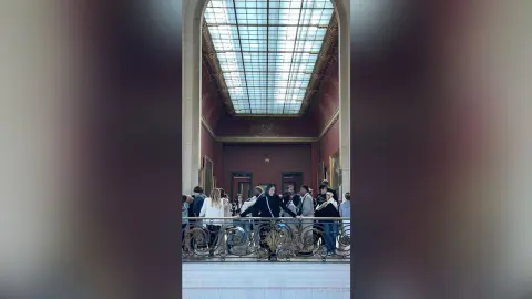 Group of tourists standing on a balcony under a grand glass ceiling in a historic classical building.