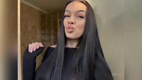 AriaVex pouts her lips while wearing a black off-the-shoulder top with her long black hair styled straight.
