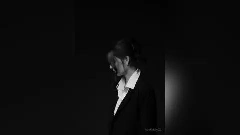 Moody black and white portrait of a woman in a white shirt and dark blazer against a dark background.