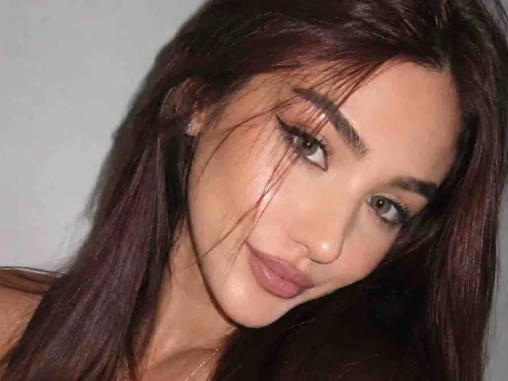 Close-up portrait of a brunette woman with winged eyeliner and glowing makeup looking into the camera.