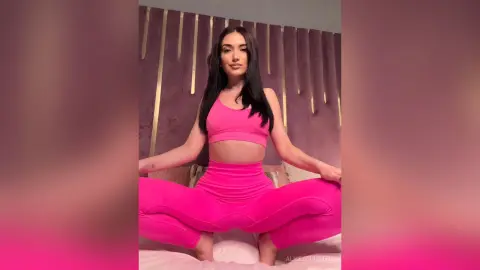 Young woman in pink yoga set sitting on a bed in a modern bedroom with a relaxed mood.