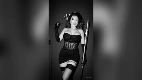 Glamorous woman in a black corset and mini dress posing in a moody black and white studio setting.