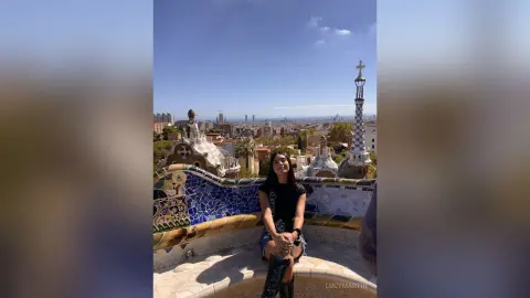 LucyMartin sits on a mosaic-tiled ledge overlooking a city skyline under a clear blue sky.