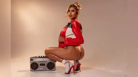 Stylish woman in a red and white jacket and white high heels posing with a vintage boombox in a studio setting.