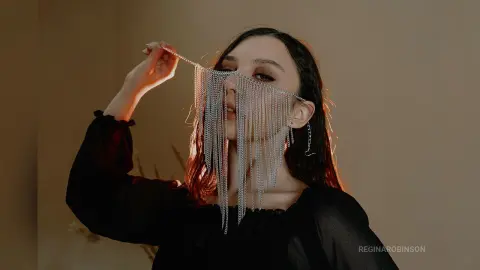 Young woman in a black blouse wearing silver chain fringe veil for a moody, artistic fashion portrait.
